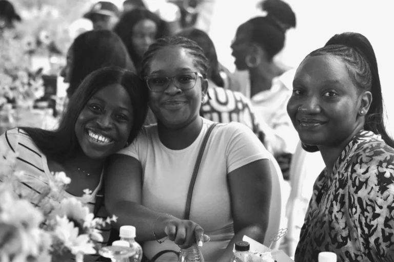 Three women in monochrome share a close, smiling group portrait at an event.