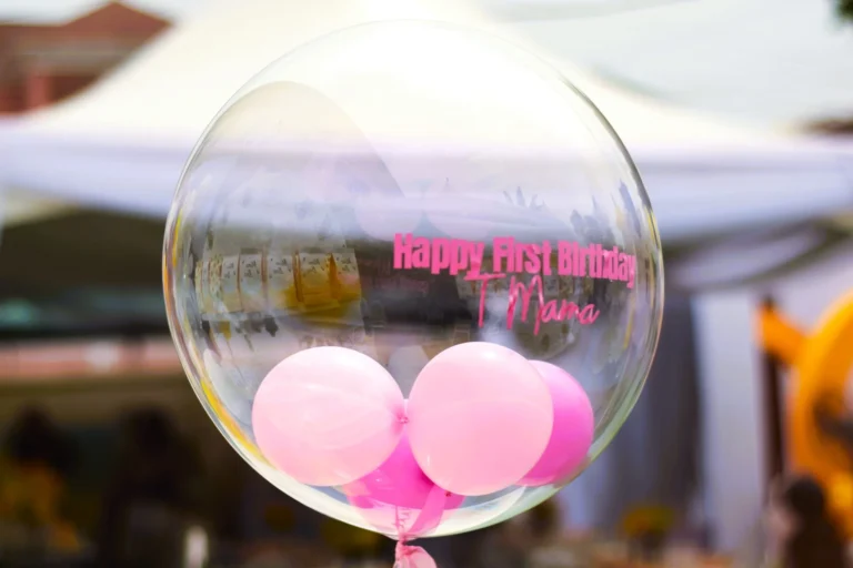 Transparent bubble balloon reads Happy First Birthday surrounded by pink balloons inside.