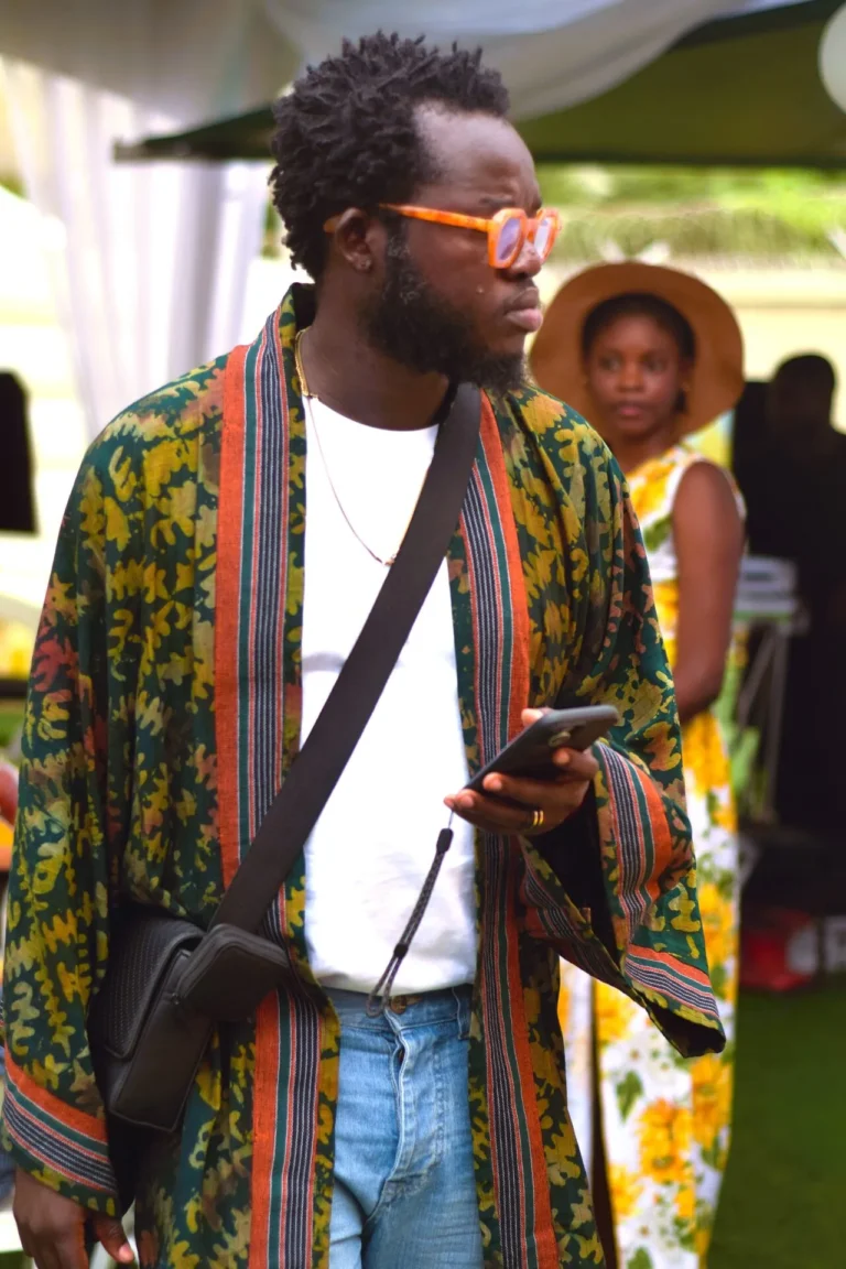 Man in colourful striped kimono and orange glasses walks past with phone in hand.