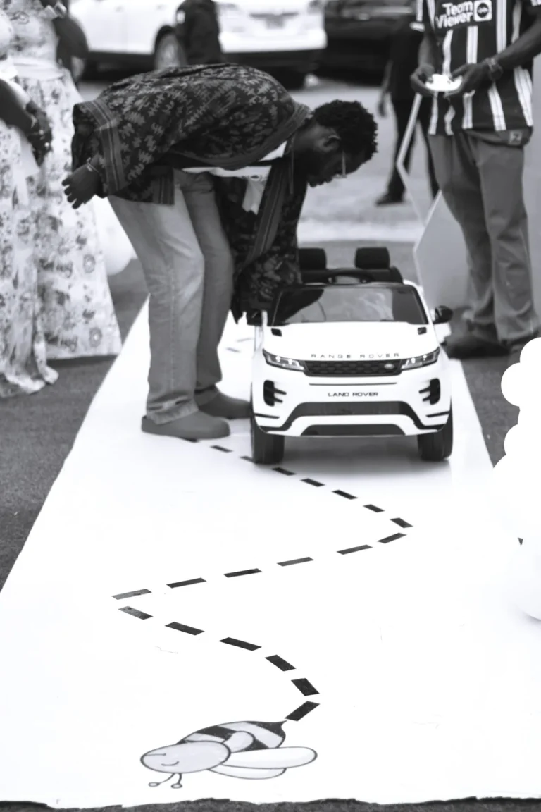 Man bends to inspect a child's Land Rover toy car on a decorated walkway.
