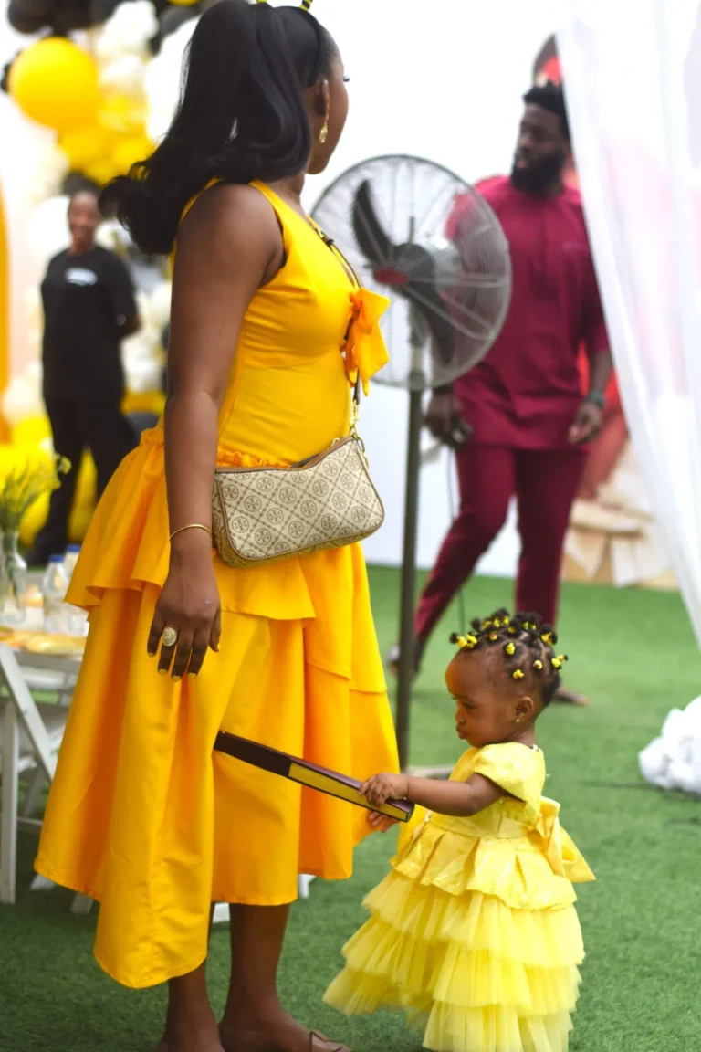 Woman in yellow dress holds hands with a tiny girl in a matching ruffled yellow dress.