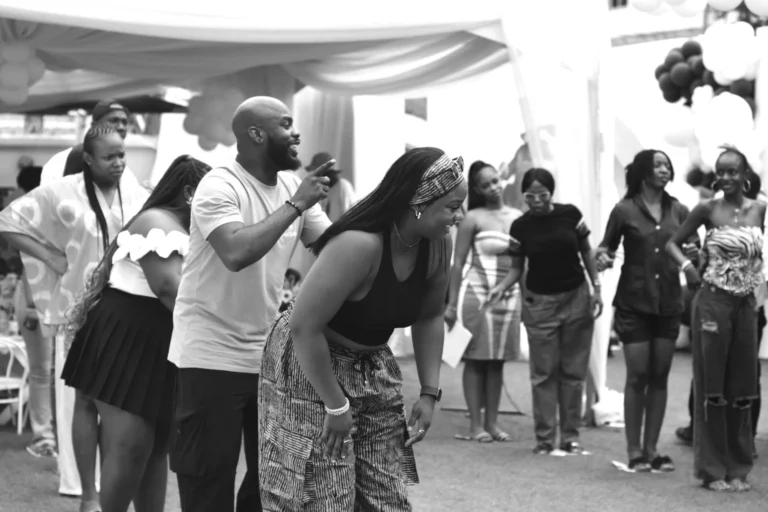 Crowd of guests dance and laugh together under a marquee in black and white.
