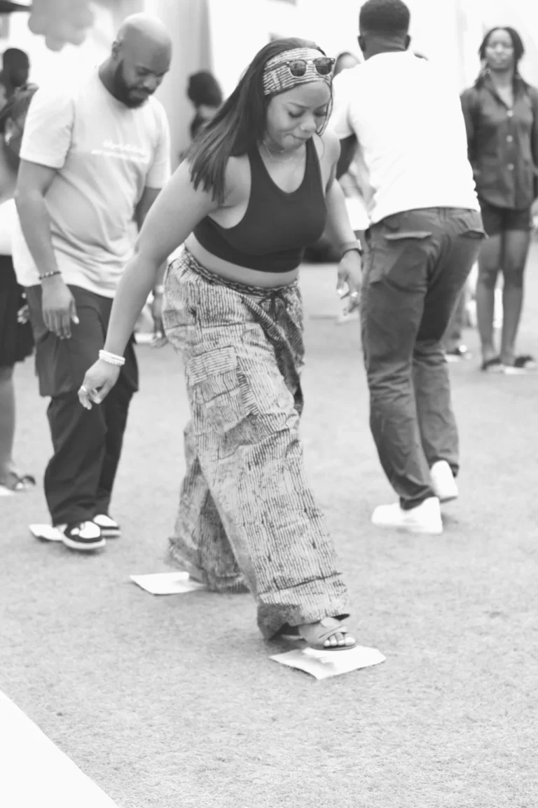 Woman dances barefoot on paper squares in a monochrome scene among other dancers.