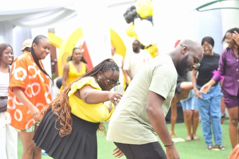 Three guests dance playfully on green turf at an outdoor celebration with yellow decor.