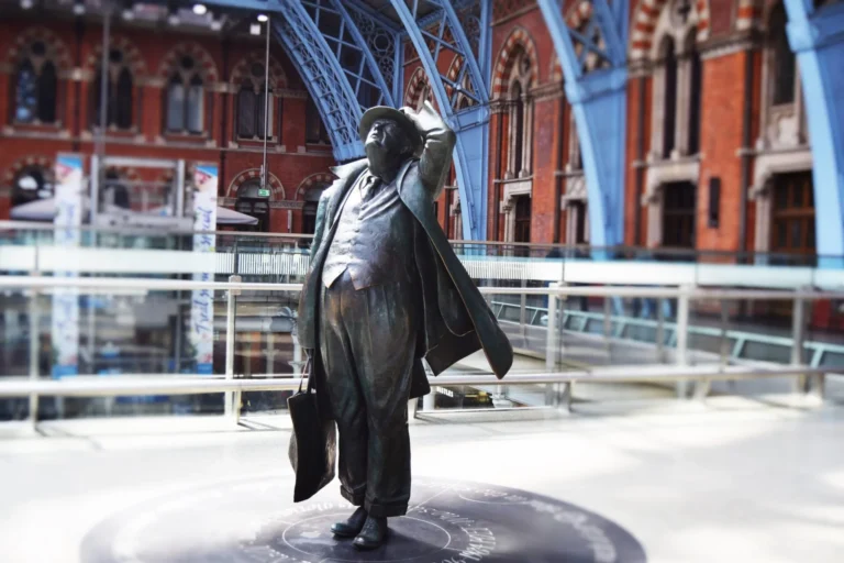 Bronze statue of John Betjeman gazing upward at the St Pancras station train shed roof.