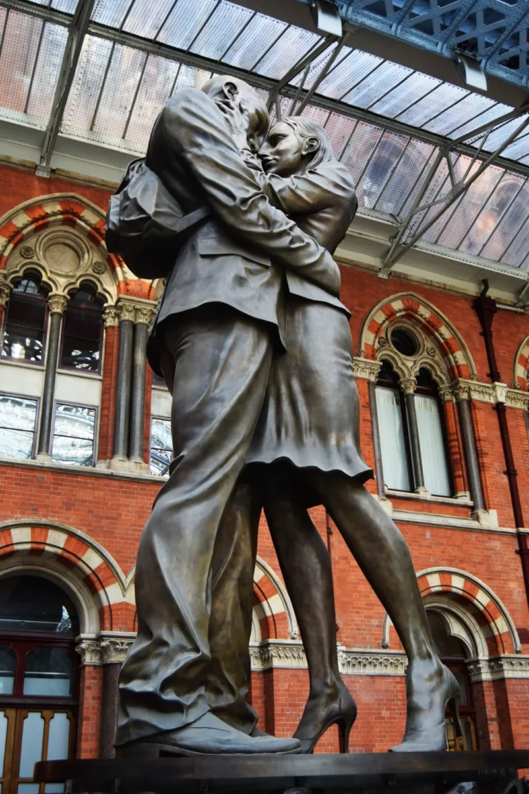 Bronze 'Meeting Place' statue of a couple embracing under the arches of St Pancras station.