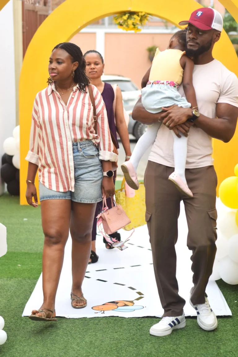 Striped-shirted woman walks alongside a man carrying a small child through a yellow arch.