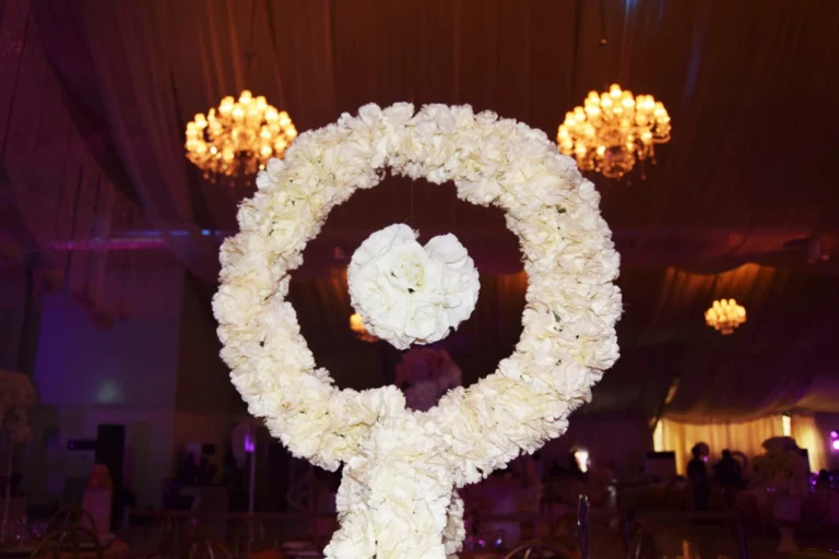 Large white floral hoop centrepiece with hanging rose ball, lit by chandeliers in a draped venue.