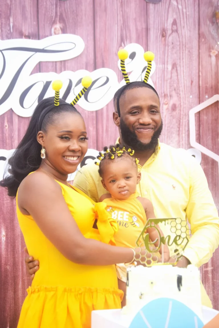 Parents in matching yellow outfits and bee antennae headbands pose with their daughter.