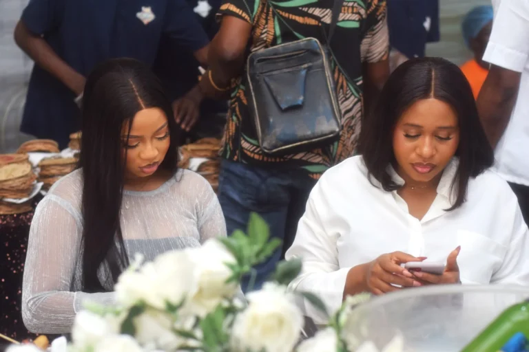 Two young women sit at a table, one looking down at her phone.