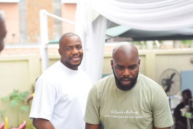 Two men chatting outdoors, one wearing a sage Art Captivates the Soul T-shirt.