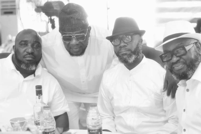 Four men in white shirts and hats pose closely together for a black-and-white portrait.