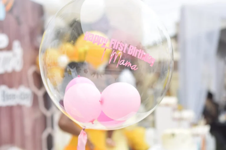 Clear bubble balloon printed Happy First Birthday Mama containing two smaller pink balloons.