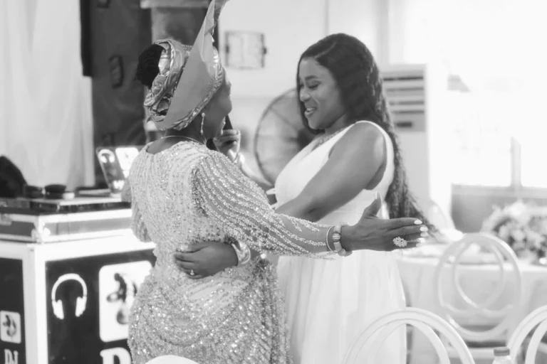 Two women embrace warmly in black and white at an event venue.