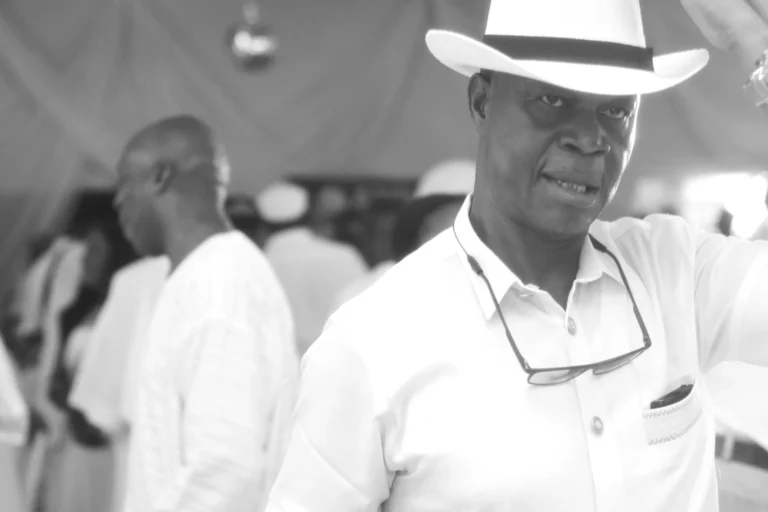 Man in white fedora and shirt poses confidently in a black-and-white candid.