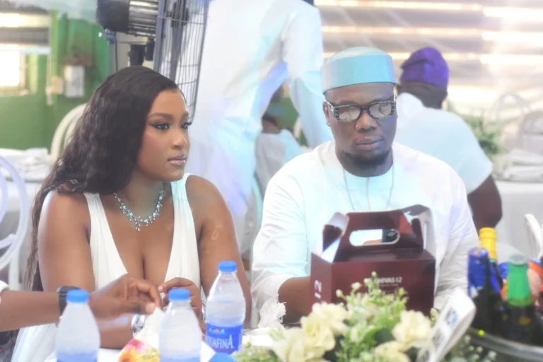 Young couple sit together at a reception table laden with bottled drinks.