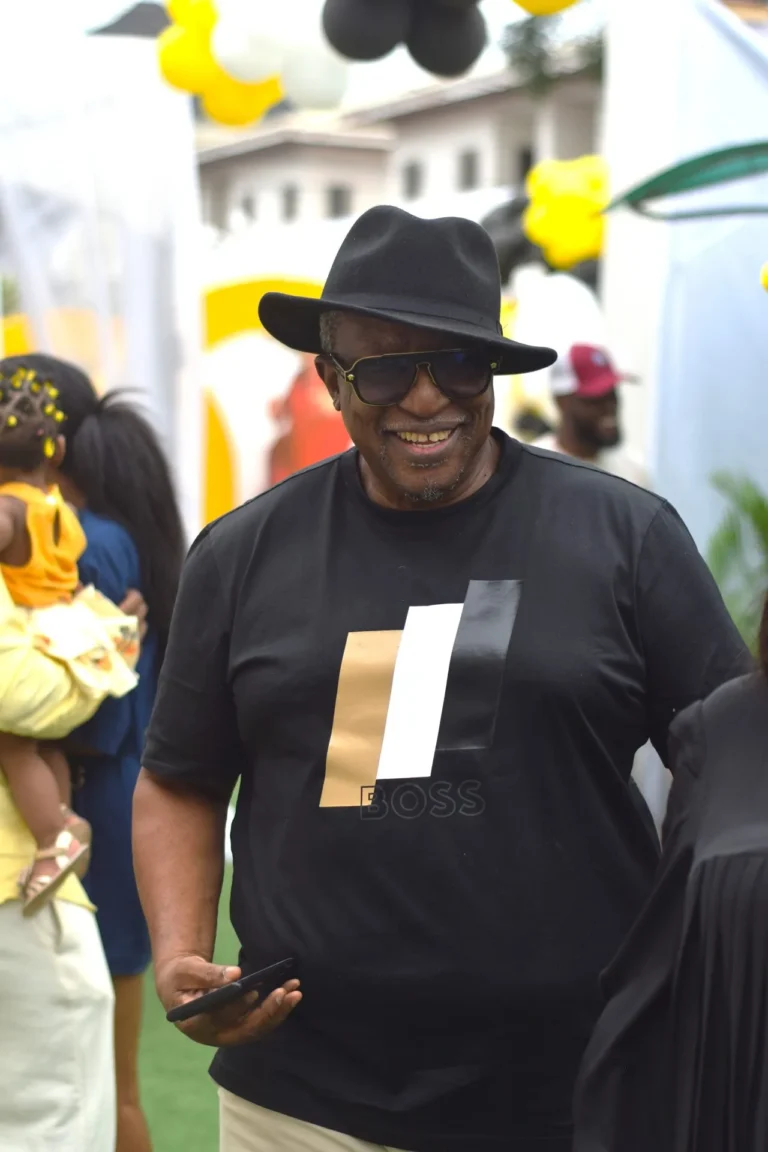Smiling older man in fedora hat and Boss T-shirt walks past balloon decorations.