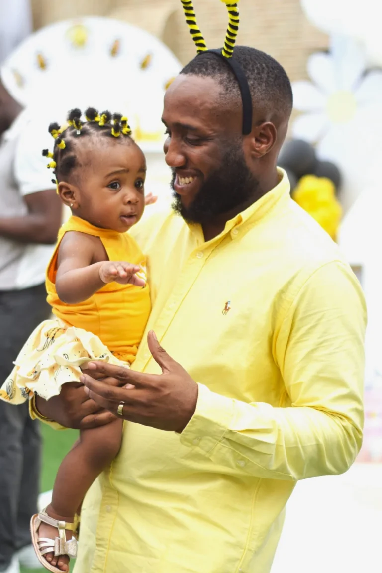 Father in yellow shirt and bee antennae holds his toddler daughter, both wearing matching outfits.