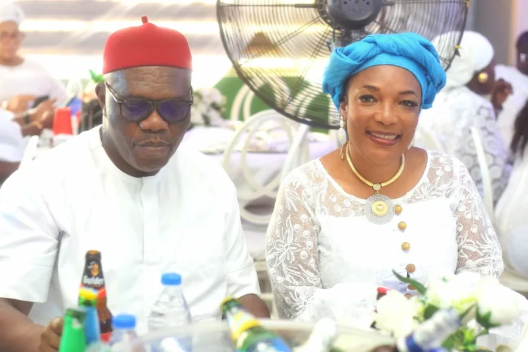 Couple in red cap and turquoise headwrap sit smiling behind a drinks table.