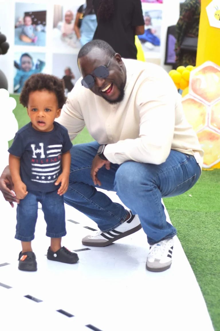 Laughing father crouches beside his young son in matching jeans by photo display boards.