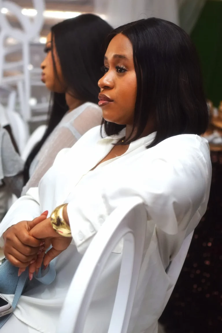 Young woman in white blouse and gold cuff sits in profile at a reception.