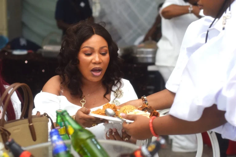 Woman in white reacts with surprise as a plate of jollof rice is served.