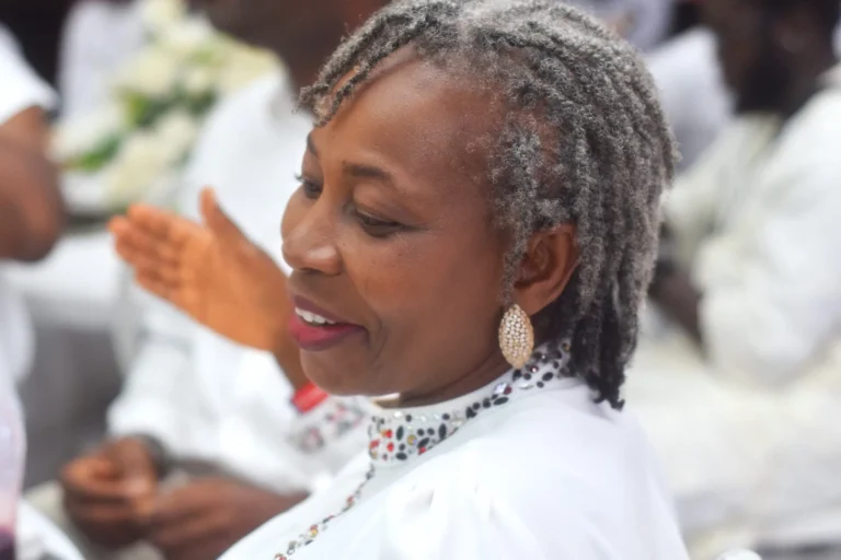 Older woman with grey locs smiles in profile, clapping at a celebration.