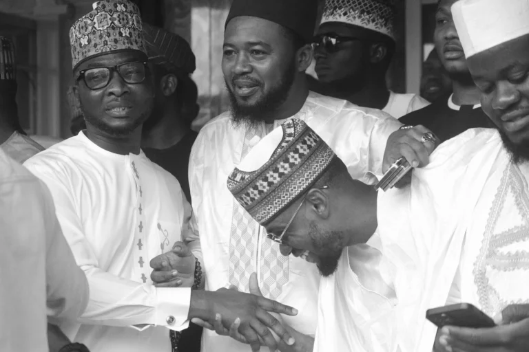 Black and white shot of men in embroidered caps laughing and clasping hands warmly.