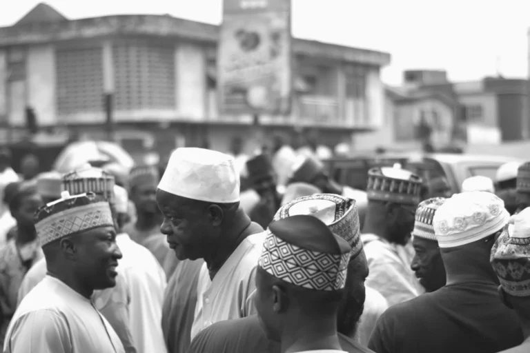 Men in embroidered caps converse on a busy street with shopfronts behind.