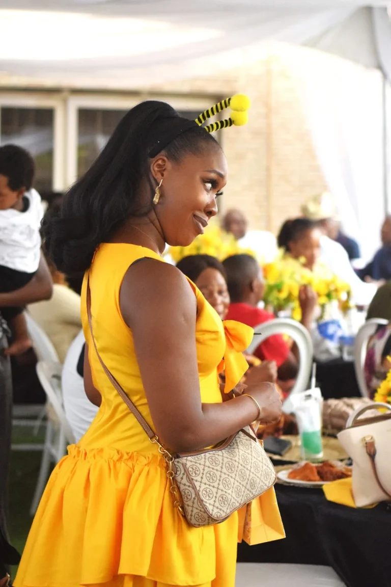 Woman in yellow ruffled dress with bee antennae mingles amongst seated guests at a tent reception.
