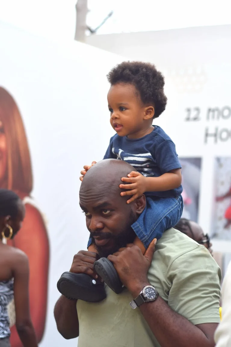 Toddler boy sits perched on his father's shoulders at an indoor celebration.