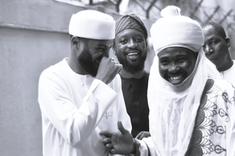 Four men in white robes share a moment of laughter outside a building.