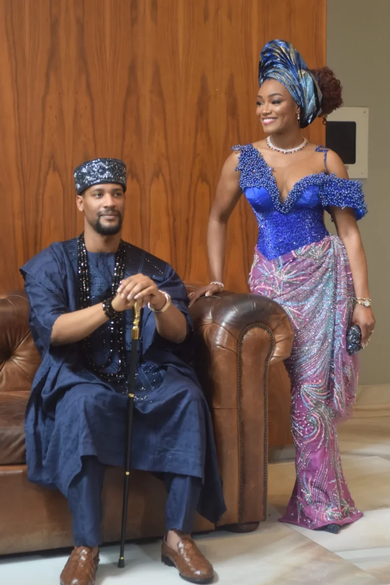 Smiling couple in coordinated navy and blue Nigerian wedding attire share a glance.