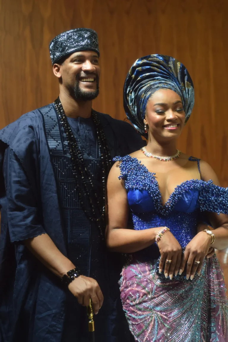 Couple stand close together in navy agbada and royal-blue Nigerian wedding outfits.