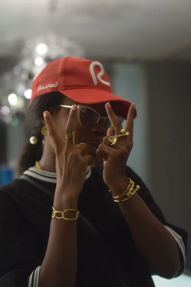 Person in red R cap throws hand signs showing stacked gold rings and bracelets.