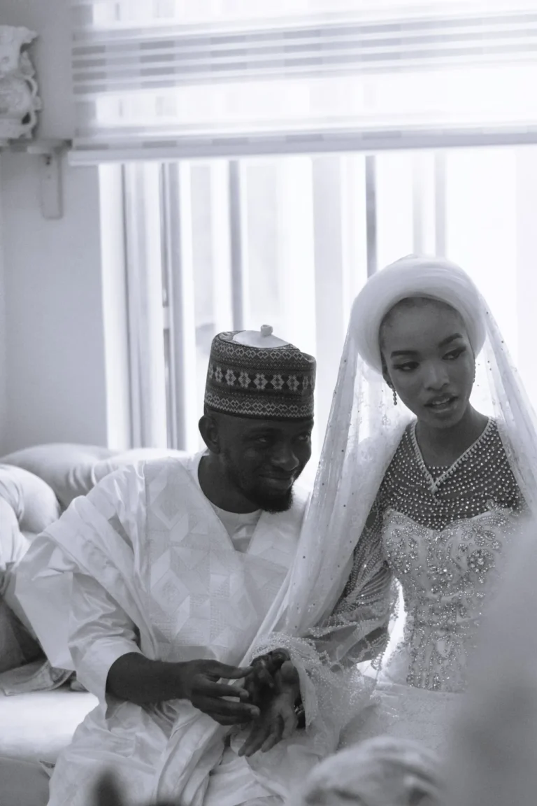 Groom in embroidered cap holds bride's hand; she wears a beaded veiled gown.