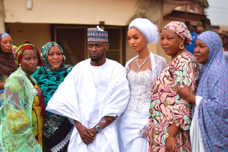 Bride and groom flanked by female relatives in colourful traditional gele headwraps.