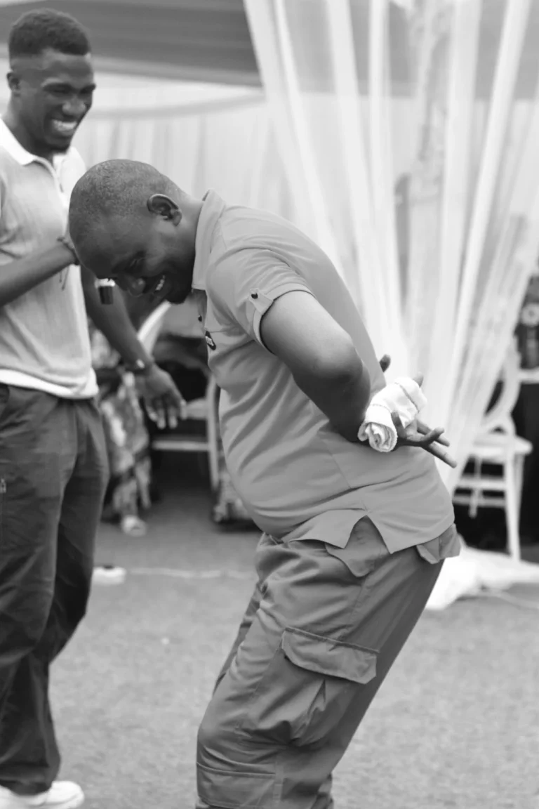 Black and white shot of a man dancing playfully, leaning forward holding a microphone behind his back.