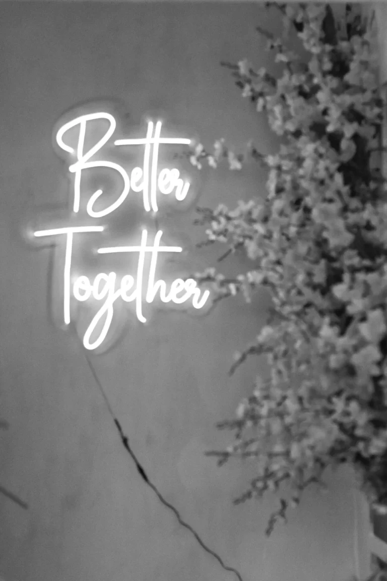 Illuminated white neon sign reading Better Together beside cherry blossom branches.
