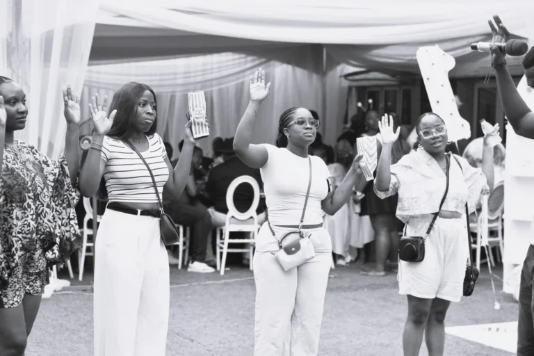 Black and white photo of four women raising their hands and dancing inside a draped marquee.