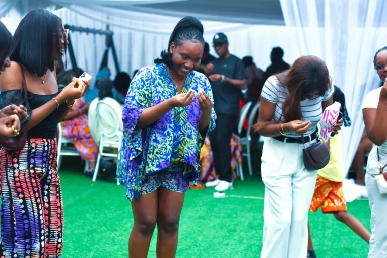 Woman in blue patterned kimono laughs as guests dance and take photos around her on green turf.