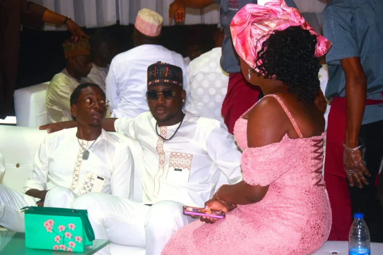 Couple in white traditional outfits chat with a woman in pink lace dress and gele.
