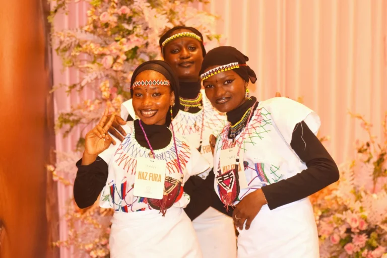 Three young women in beaded headbands and matching tops pose smiling together.